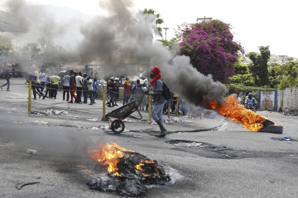 A man pushes a wheelbarrow past burning tires during a protest demanding the resignation of Prime Minister Ariel Henry, in Port-au-Prince, Haiti, Thursday, March 7, 2024. (AP Photo/Odelyn Joseph)
