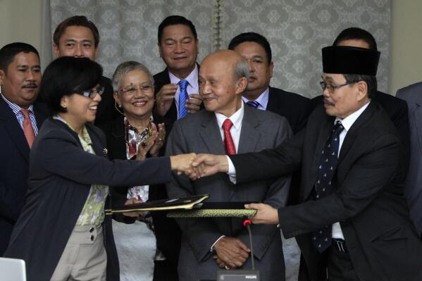 FILE - Miriam Coronel-Ferrer, front left, chairperson of Philippine Government Peace Panel, and Mohagher Iqbal, front right, chief negotiator for the Moro National Liberation Front (MNLF), exchange signed documents as Malaysian facilitator Abdul Ghafar Tengku Mohamed, front center, witnesses after the 43rd GPH-MILF Exploratory Talks in Kuala Lumpur, Malaysia on Jan. 25, 2014. Foreign peacekeepers credited with helping ease years of bloody fighting between government forces and Muslim rebels have left the southern Philippines after officials terminated their presence but talks are underway to allow their possible return, officials and the rebels said Friday, July 15, 2022. (AP Photo/Lai Seng Sin, File)