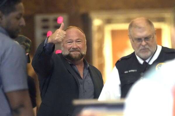 Right-wing conspiracy theorist Alex Jones gives a thumbs-up as he goes through security at the federal courthouse after arriving for a hearing in front of a bankruptcy judge Friday, June 14, 2024, in Houston. The judge is expected to rule on whether to liquidate Jones' assets to help pay the $1.5 billion he owes for his false claims that the Sandy Hook Elementary School shooting was a hoax. (AP Photo/David J. Phillip)