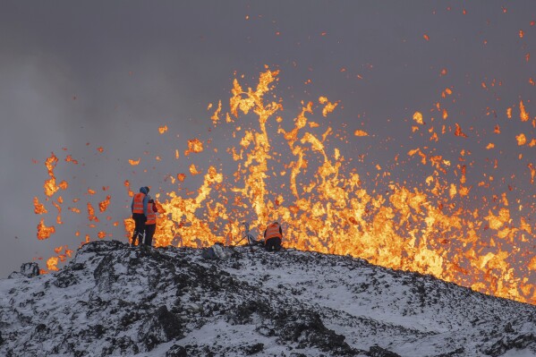 Scientist of the University of Iceland take measurements and samples standing on the ridge in front of the active part of the eruptive fissure of an active volcano in Grindavik on Iceland's Reykjanes Peninsula, Tuesday, Dec. 19, 2023. (AP Photo/Marco Di Marco)