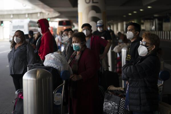 Travelers wait for a shuttle but to arrive at the Los Angeles International Airport in Los Angeles, Monday, Dec. 20, 2021. The Los Angeles County Department of Public Health reported more than 3,500 new cases of COVID-19 on Sunday as the number of daily new cases tripled over the week. (AP Photo/Jae C. Hong)