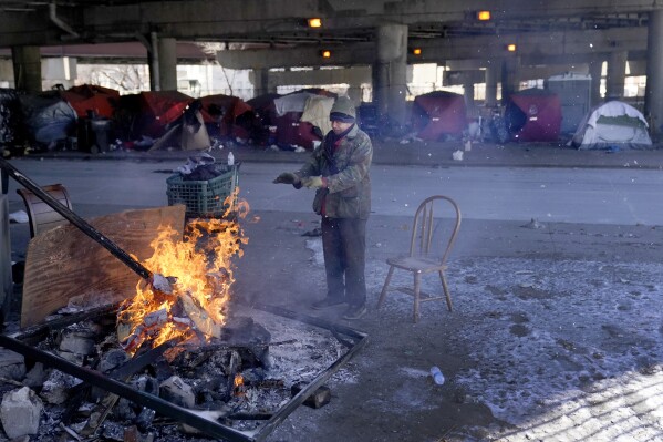 An elderly man warms his hands by the fire he created all the plan in which by the boulevard from a homeless encampment beneath a critical interstate freeway Tuesday, Jan. 16, 2024, in Chicago. Hundreds and thousands of American citizens face below-zero temperatures as storms bring a blast of Arctic air, snow and ice. (AP Describe/Charles Rex Arbogast)