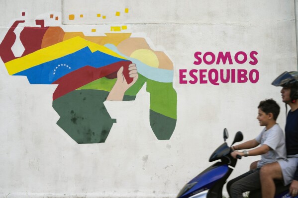 A youth drives a motorcycle in front of a mural of a map of Venezuela with the Essequibo territory, a swath of land administered and controlled by Guyana but claimed by Venezuela, in the 23 de Enero neighborhood of Caracas, Venezuela, Dec. 11, 2023. (AP Photo/Matias Delacroix, File)