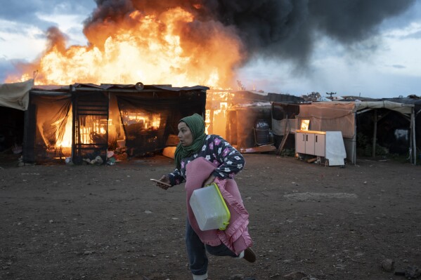A woman runs past burning shacks during a fire before an eviction by police officers in Almeria, Spain, Jan. 30, 2023. (AP Photo/Santi Donaire)