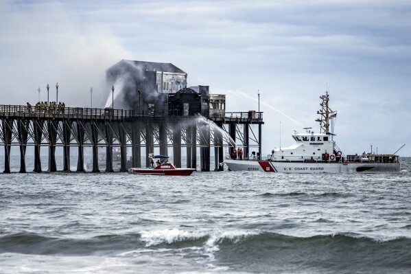 Firefighters battle a fire on a landmark wooden pier in Oceanside, Calif., Thursday, April 25, 2024. The stubborn fire at the end of a landmark wooden pier on the Southern California coast was contained early Friday, authorities said. (Patrick Trolan/Media Baller, via AP)