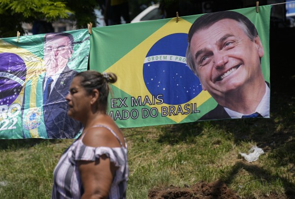 A woman walks past a banner featuring the Brazilian national flag and an image of former President Jair Bolsonaro with a message that reads in Portuguese: "Ex, most beloved of Brazil", in Rio de Janeiro, Brazil, Saturday, March 16, 2024. (AP Photo/Silvia Izquierdo)