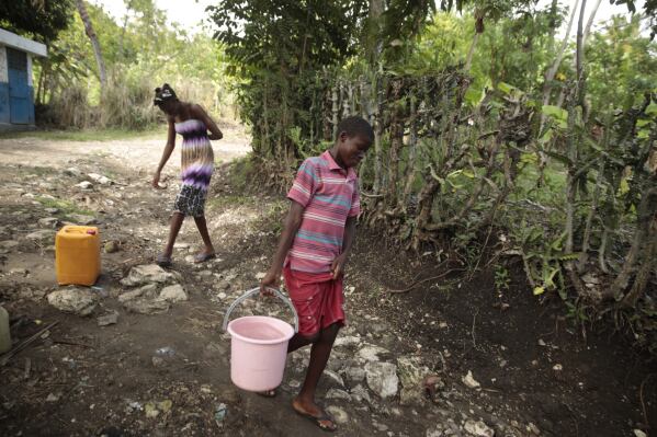 Siblings Mylouise Veillard, left, and Myson walk home with water they collected from a well, for cooking, cleaning and drinking, in a rural area of Saint-Louis-du-Sud, Haiti, Thursday, May 25, 2023. The siblings were considered “poverty orphans" for three years until they were reunited with their mother, Renèse Estève, who had dropped them off at an orphanage where she believed they'd get better care. Their mother brought them home after she was startled at the weight they had lost, convinced they'd be better off living in grinding poverty. (AP Photo/Odelyn Joseph)