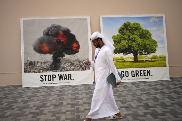 A person walks past signs that read "stop war" and "go green" at the COP28 U.N. Climate Summit, Dec. 8, 2023, in Dubai, United Arab Emirates. (AP Photo/Rafiq Maqbool)