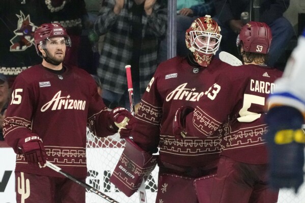 Arizona Coyotes goaltender Connor Ingram, center, celebrates a win against the St. Louis Blues with Coyotes left wing Michael Carcone (53) and Coyotes center Alexander Kerfoot, left, as time expires in the third period of an NHL hockey game Saturday, Dec. 2, 2023, in Tempe, Ariz. The Coyotes won 4-1. (AP Photo/Ross D. Franklin)