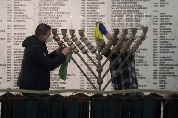 Workers in the Polish parliament clean up a menorah after a far-right lawmaker grabbed a fire extinguisher and put out a candle, disturbing a celebration of the Jewish holiday of Channukah, in Warsaw, Poland, on Tuesday Dec. 12, 2023. (AP Photo/Czarek Sokolowski)