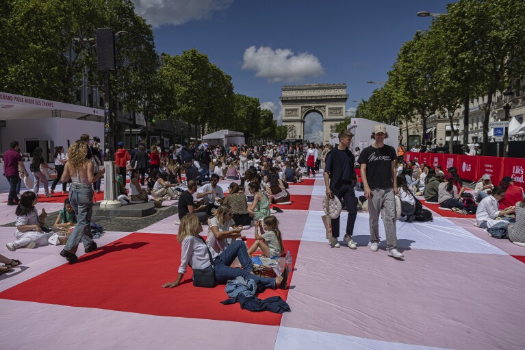 Die Menschen essen ihr Mittagessen im Rahmen eines riesigen Picknicks entlang der Champs-Elysées vor dem Arc de Triomphe, organisiert vom Champs-Elysées-Komitee, Sonntag, 26. Mai 2024 in Paris.  (AP Photo/Aurelien Morisard)