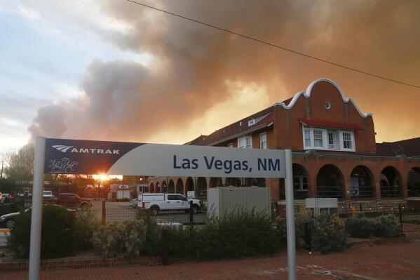 A sunset seen through a wall of wildfire smoke from the Amtrak train station in Las Vegas, N.M., on Saturday, May 7, 2022. The Castañeda Hotel, right, hosted meals for residents and firefighters this week with sponsorships from restaurants and other businesses. (AP Photo/Cedar Attanasio)