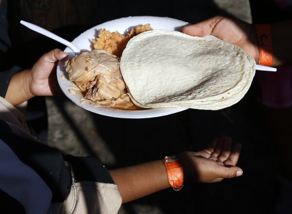 
              A young Central American migrant receives a free meal of chicken, rice and tortillas at a shelter for migrants in Tijuana, Sunday, Nov. 18, 2018. While many in Tijuana are sympathetic to the plight of Central American migrants and trying to assist, some locals have shouted insults, hurled rocks and even thrown punches at the migrants. (AP Photo/Marco Ugarte)
            