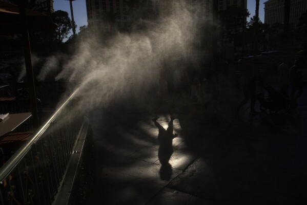 People walk along the Las Vegas Strip by cooling misters Thursday, July 13, 2023, in Las Vegas. (AP Photo/John Locher)