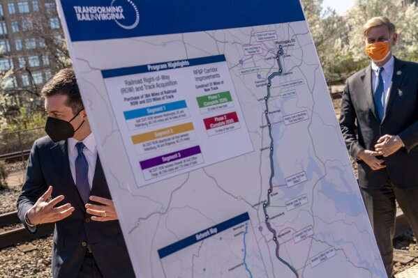 A poster depicting transportation plans is visible as Transportation Secretary Pete Buttigieg, left, and Rep. Don Beyer, D-Va., right, depart following a news conference to announce the expansion of commuter rail in Virginia at the Amtrak and Virginia Railway Express (VRE) Alexandria Station, Tuesday, March 30, 2021, in Alexandria, Va. (AP Photo/Andrew Harnik)