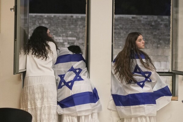Israeli girls covered with Israeli flags overlooking the Western Wall, the holiest site where Jews can pray, during Jerusalem Day, an Israeli holiday celebrating the capture of east Jerusalem in the 1967 Midea st war, in Jerusalem' Old City, Monday, May 26, 2025. (AP Photo/Maya Alleruzzo)