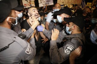 Israeli police officers push a protester outside Prime Minister's residence in Jerusalem, Tuesday, July 14, 2020. Thousands of Israelis on Tuesday demonstrated outside the official residence of Prime Minister Benjamin Netanyahu, calling on the embattled Israeli leader to resign as he faces a trial on corruption charges and grapples with a deepening coronavirus crisis. The signs reads "You are detached. We are fed up".(AP Photo/Ariel Schalit)
