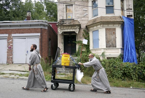 
              Rev. Giuseppe Siniscalchi, right, and Brother Peter Anthony Curtis push a cart with cold drinks through the streets of Newburgh, N.Y., Wednesday, Oct. 3, 2018. The brothers use the cart, usually filled with drinks or snacks, as a way to strike up conversations with people. (AP Photo/Seth Wenig)
            