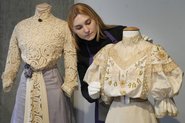 A costume handler arranges Helena Bonham Carter's costume as Lucy Honeychurch in the film A Room With a View 1985 as it is displayed at Kerry Taylor Auctions in London, Tuesday, Feb. 27, 2024. The costume estimated at 800-1,000 UK Pounds (1,000-1,300 US Dollars) is one of 69 that will be for auction in the Lights Camera Auction event on March 5. The costumes have been donated by Cosprop in support of The Bright Foundation, an arts education charity, established and funded by John Bright, to provide life-enhancing, creative experiences for children and young people facing disadvantage. (AP Photo/Kirsty Wigglesworth)