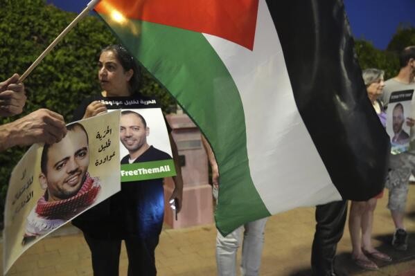 Protesters gather with a Palestinian flag outside the hospital where Palestinian Khalil Awawdeh, pictured in the placards, a prisoner in Israel on hunger strike, is now clinging to life in Be'er Yaakov, Saturday, Aug. 13, 2022. Arabic on the placard reads, "Freedom for Khalil Awawdeh." His family says Awawdeh has refused food to draw attention to his detention by Israel without trial or charge. (AP Photo/Tsafrir Abayov)