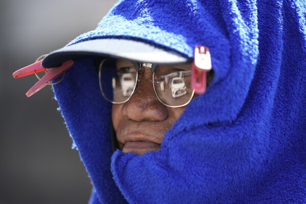 Parking attendant Andy Tinto uses laundry clips to put a blue towel over his cap to protect himself from the sun in Manila, Philippines on Monday, April 29, 2024. (AP Photo/Aaron Favila)