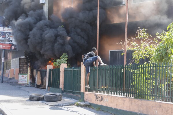 A man climbs the fence of an office of Haiti's power company set on fire during a protest to demand the resignation of the Prime Minister Ariel Henry in Port-au-Prince, Haiti, Friday, March 1, 2024. (AP Photo/Odelyn Joseph)