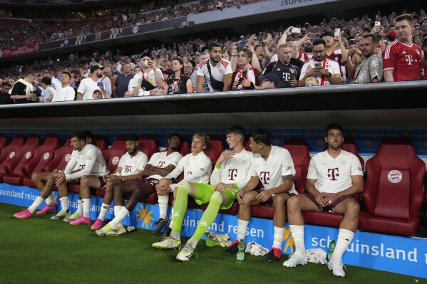 Bayern's Harry Kane, right, and his new teammates sit on the bench prior the German Super Cup final between FC Bayern Munich and RB Leipzig at the Allianz Arena stadium in Munich, Germany, Saturday, Aug. 12, 2023. (AP Photo/Matthias Schrader)