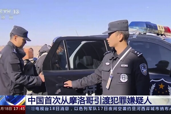 In this image taken from video footage run by China's CCTV, a fugitive accused of economic crimes known by his surname Luo is taken away by Chinese police officer after being extradited from Morocco and arriving at the airport in Shanghai , China, Saturday, Nov. 18, 2023. A Chinese man wanted for allegedly embezzling millions of yuan (hundreds of thousands of dollars) from his company and then fleeing to Morocco has been extradited back to China, State broadcaster CCTV showed the man being handcuffed and led to a police car after getting off a plane on Saturday, (CCTV via AP)