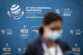 FILE - A person walks past the WTO Ministerial MC12 logo before the opening of the 12th Ministerial Conference at the headquarters of the World Trade Organization in Geneva, Switzerland on June 12, 2022. The World Trade Organization has rejected the 2018 import taxes that then-President Donald Trump imposed on foreign steel and aluminum, saying they violated global trade rules. (Martial Trezzini/Keystone via AP, File)