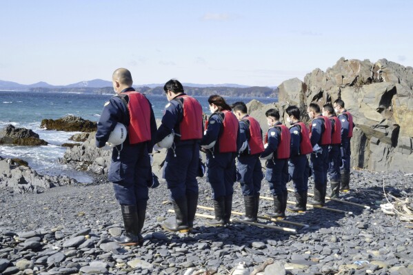 Police officers offer a silent prayer ahead of their search operation for the missing persons in Minamisanriku, Miyagi prefecture, northern Japan Monday, March 11, 2024. Japan marked the 13th anniversary of the massive earthquake, tsunami and nuclear disaster. (Kyodo News via AP)
