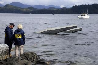 FILE - In this photo provided by the National Transportation Safety Board, NTSB investigator Clint Crookshanks, left, and member Jennifer Homendy stand near the site of some of the wreckage of the DHC-2 Beaver, Wednesday, May 15, 2019, that was involved in a midair collision near Ketchikan, Alaska, a couple of days earlier.  The pilots of two Alaskan sightseeing planes that collided in midair couldn't see the other aircraft because airplane structures or a passenger blocked their views, and they didn't get electronic alerts about close aircraft because safety systems weren't working properly. That's what the staff of the National Transportation Safety board found in their investigation. (Peter Knudson/NTSB via AP)