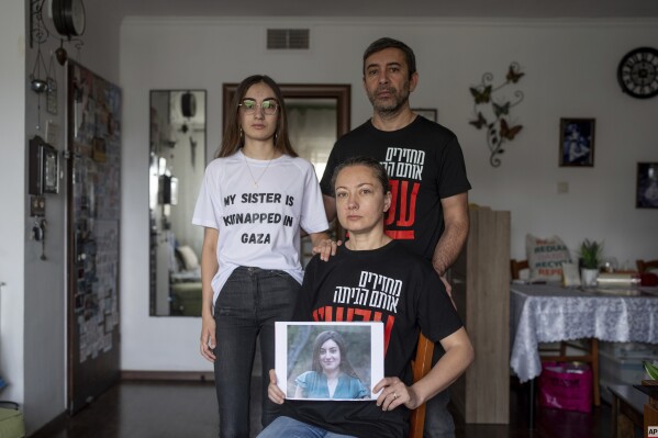 The Ariev family, parents Albert and Ira and their daughter Sasha, hold up a portrait of young soldier Karina Ariev in their family house in Jerusalem, Sunday, Oct. 29, 2023. Ariev, an Israeli soldier, was abducted by Hamas militants from her base during her mandatory military service during the militant group's unprecedented attack on Israel on Oct. 7 that resulted in the killing of 1,400 people and the abduction of over 220. (AP Photo/Ohad Zwigenberg).