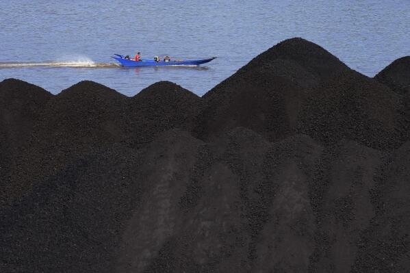 A boat cruises past a coal barge on Mahakam River in Samarinda, East Kalimantan, Indonesia, Monday, Dec. 19, 2022. Indonesia, one of the world's largest coal-producing countries, has agreed to drastically reduce its reliance on fossil fuels in the coming decades. (AP Photo/Dita Alangkara)