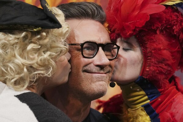 Harvard University's Hasty Pudding Theatricals Man of the Year Jon Hamm is kissed by character actors while holding his award, Friday, Jan. 31, 2025, in Cambridge, Mass. (AP Photo/Charles Krupa)