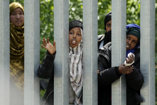 A group of migrant women stand behind a metal barrier trying to cross into Poland, in Bialowieza Forest, eastern Poland, on Wednesday, May 29, 2024. Poland’s Prime Minister Donald Tusk says its forces would fortify the border with Belarus after a soldier was seriously wounded with a knife by a migrant. (AP Photo/Czarek Sokolowski)