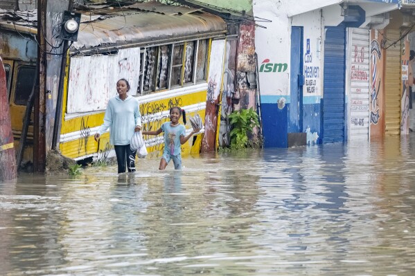 People walk through a street flooded by the rains of Tropical Storm Franklin in Santo Domingo, Dominican Republic, Tuesday, Aug. 22, 2023. (AP Photo/Ricardo Hernandez)