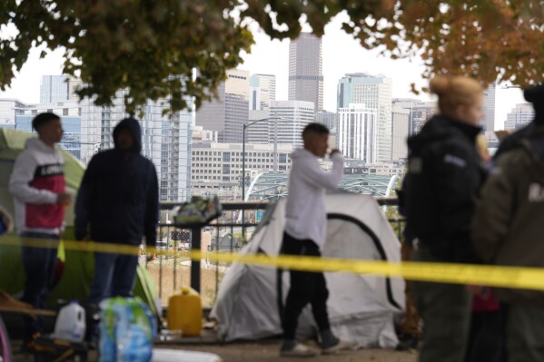 Occupants wait to see how police officers work during a city-sponsored sweep of an encampment overlooking the city skyline on Diamond Hill Wednesday, Nov. 1, 2023, in Denver. The sweep was just one of several staged in various locations across the Mile High City. (AP Photo/David Zalubowski)