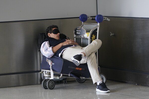 FILE - A traveler takes a nap as he waits for a ride outside Miami International Airport, Friday, July 1, 2022, in Miami. The Gallup survey, released Monday, April 15, 2024, says that a majority of Americans say they would feel better if they could have more sleep. But in the U.S., where the ethos of grinding and pulling yourself up by your own bootstraps is ubiquitous, getting enough sleep can seem like a dream. (AP Photo/Wilfredo Lee, File)