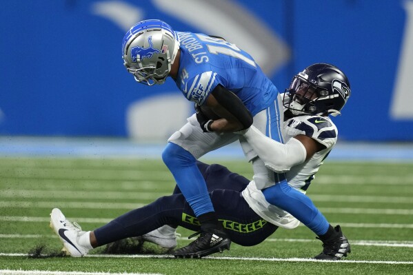 Detroit Lions wide receiver Amon-Ra St. Brown (14) is tackled by Seattle Seahawks safety Julian Love (20) after catching a pass during the first half of an NFL football game, Sunday, Sept. 17, 2023, in Detroit. (AP Photo/Paul Sancya)