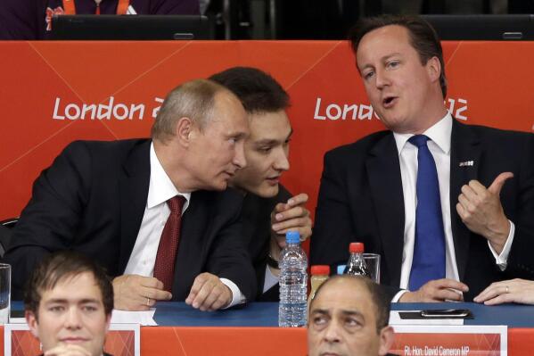 FILE - Russian President Vladmir Putin, left, and British Prime Minister David Cameron watch the judo during the men's 100-kg judo competition at the 2012 Summer Olympics, Aug. 2, 2012, in London. The International Judo Federation has removed the titles and jobs Vladimir Putin and long-time Kremlin-supporting oligarch Arkady Rotenberg held at the organization, the governing body said in a statement late Sunday March 6, 2022. (AP Photo/Ng Han Guan, File)