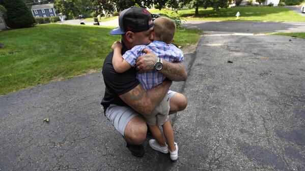 Mike Gilpatrick, who as a teenager was incarcerated at the Youth Development Center, embraces his son, who just completed his first day of school, outside their home, Wednesday, Sept. 8, 2021, in Nashua, N.H. Gilpatrick, 38, filed a lawsuit Monday Sept. 13,  alleging he was physically and sexually abused at the former YDC in Manchester, which has been the target of a criminal investigation since 2019 and is slated to close in 2023. (AP Photo/Charles Krupa)