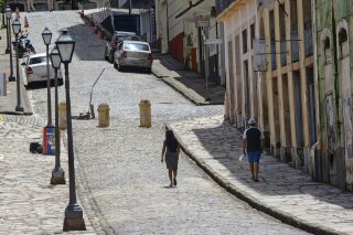 People walk in an empty street during a lockdown imposed by the government to help stop the spread of the new coronavirus in the historic district of downtown Sao Luis, in the northeastern state of Maranhao, Brazil, Tuesday, May 5, 2020. The capital of tropical Maranhão state ground largely to a halt Tuesday, becoming the first major Brazilian city to enter a lockdown in the hopes of preventing the coronavirus pandemic from overwhelming the health care system of one of the country's poorest states. (Douglas Junior/Futura Press via AP)