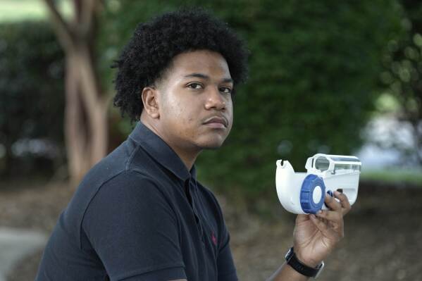 Camden Alderman, 21, who has a rare disease called Wiskott-Aldrich syndrome, holds with an infusion pump he uses near his home in Greensboro, N.C., Wednesday, June 12, 2024. When he was a toddler, doctors removed his spleen because of uncontrolled bleeding. As a young boy, he wound up in the hospital many times and was told he couldn’t play baseball. (AP Photo/Chuck Burton)