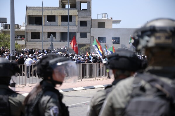 Israeli police in riot gear stand near Druze protesters as thousands took part in the demonstrations against the construction of massive wind turbines in the Golan Heights, Wednesday, June 21, 2023. Israeli police fired tear gas, sponge-tipped bullets and a water cannon during the mass demonstrations by Druze Arabs — a rare burst of violence in the normally quiet area. (AP Photo/Fadi Amun)