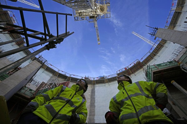 FILE - Employees look up at the construction site of Hinkley Point C nuclear power station in Somerset, England, Tuesday, Oct. 11, 2022. A major nuclear plant that Britain’s government hopes will generate affordable, low-carbon energy could cost up to 46 billion pounds, or $59 billion, and the completion date could be delayed to after 2029. The U.K. government says nuclear projects like the Hinkley Point C plant is a key part of its plans to ensure greater energy independence and achieve its “net zero” by 2050 strategy. (AP Photo/Kin Cheung, File)