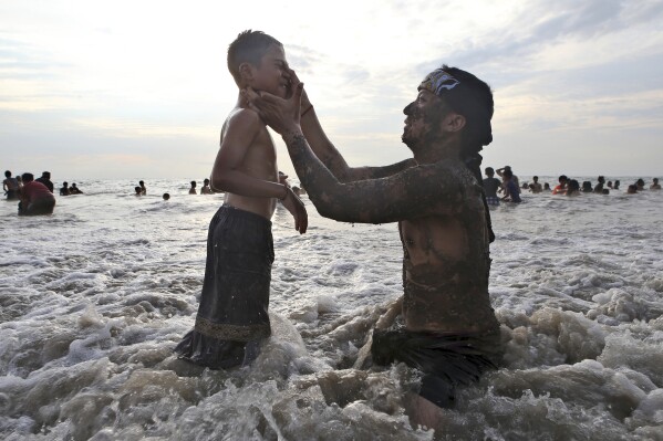 A man helps a child clean off mud from a mangrove forest after a mud bath purification ritual, in the Indian Ocean in Bali, Tuesday, March 12, 2024. The mud bath was part of Balinese Hindu New Year celebrations. (AP Photo/Firdia Lisnawati)