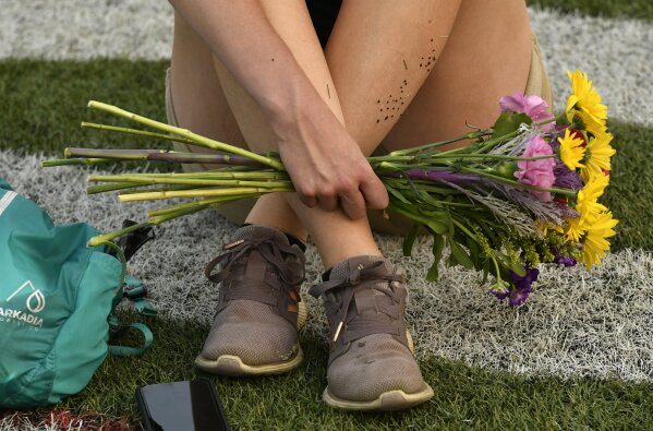 A woman holds a bouquet of flowers while seated on the artificial turf of the football stadium at the Montbello Recreation Center during an event, Gathering in Gratitude presented by Motherhood, held to honor the memory of Elijah McClain, in Denver on Sunday, Aug. 23, 2020. McClain died after being stopped by police last year in the suburb of Aurora. (Helen H. Richardson/The Denver Post via AP)