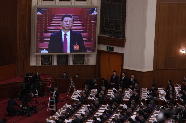 Chinese President Xi Jinping, on screen, listens to the opening remark by Chinese Premier Li Qiang during the opening session of the National People's Congress (NPC) at the Great Hall of the People in Beijing, China, Tuesday, March 5, 2024. (AP Photo/Andy Wong)