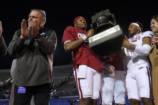 Arkansas coach Sam Pittman, left, applauds as quarterback KJ Jefferson, center, and defensive back Simeon Blair (15) attempt to hoist overhead the trophy following the team's win over Kansas in the Liberty Bowl NCAA college football game, Wednesday, Dec. 28, 2022, in Memphis, Tenn. Arkansas won 55-53 in three overtimes. (AP Photo/Rogelio V. Solis)