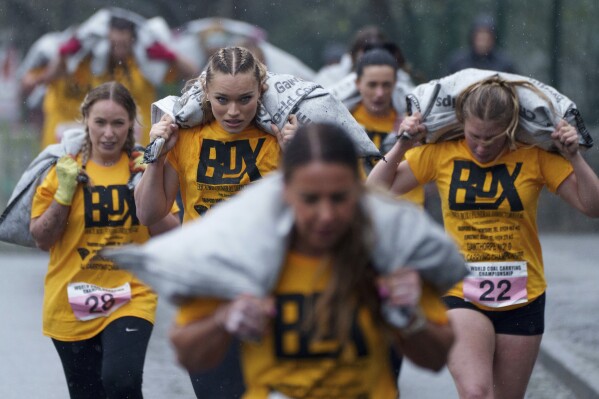 Women's race competitors, including Jodie Ounsley, center, who plays Fury in the British TV show "Gladiators," run with a 20kg sack of coal over a 1.1km course during the World Coal Carrying Championships in Ossett, West Yorkshire, England, Monday, April 21, 2025. (AP Photo/Jon Super)